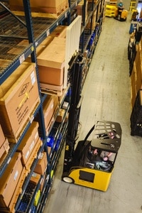 A reach truck getting goods from a shelf in a warehouse.
